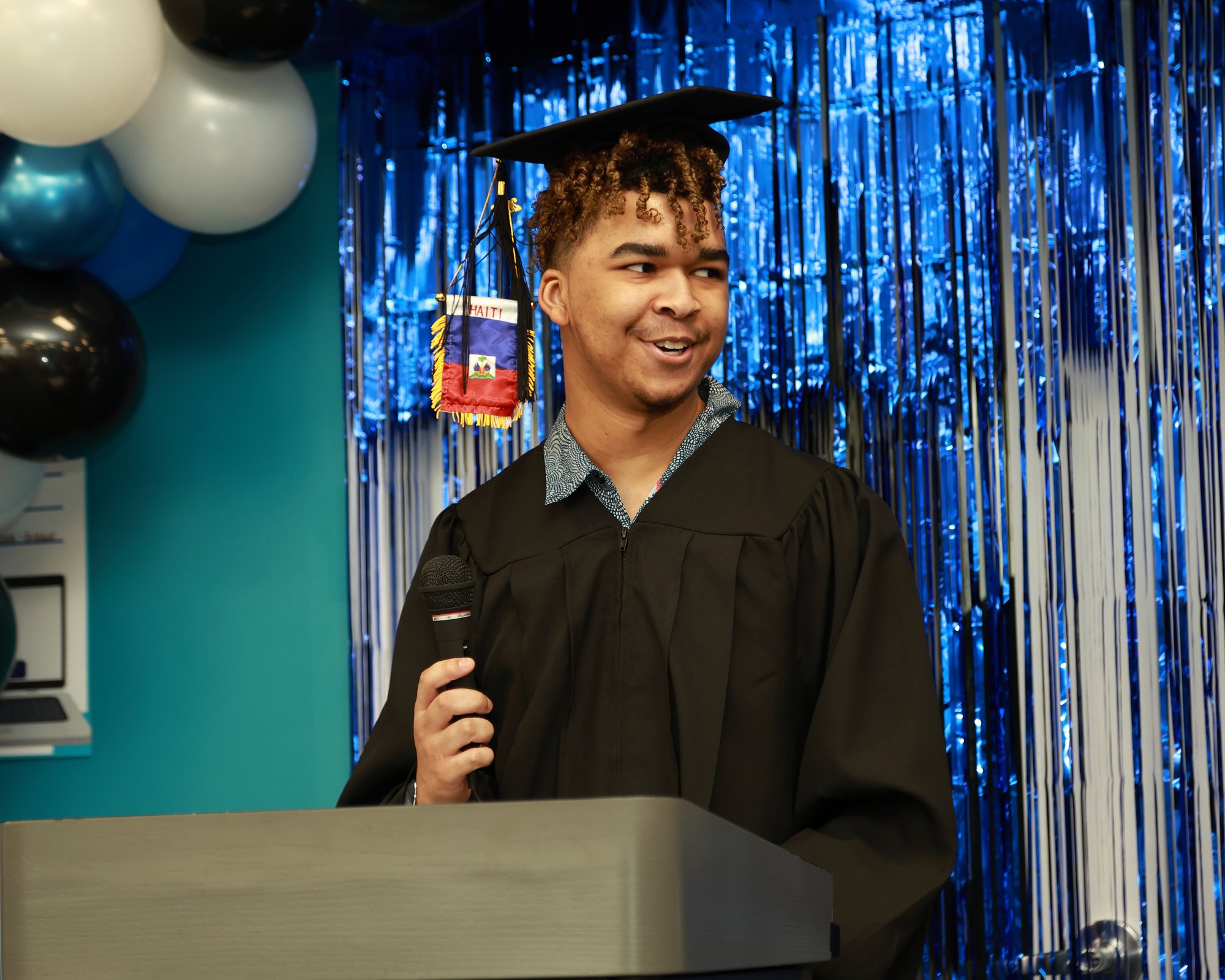 Kaiden Harvey stands in graduation cap and gown holding microphone.