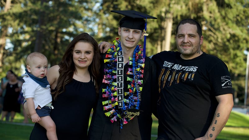 Graduate smiles in cap and gown, flanked by family members