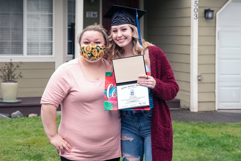Student holds diploma and poses with her mother outside of home