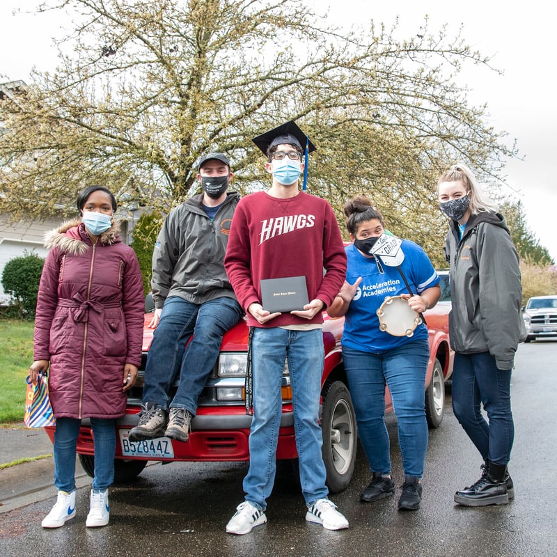 Student in mask stands by car surrounded by family