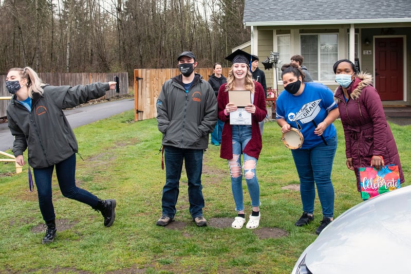 Student celebrates success in front yard, surrounded by supportive loved ones