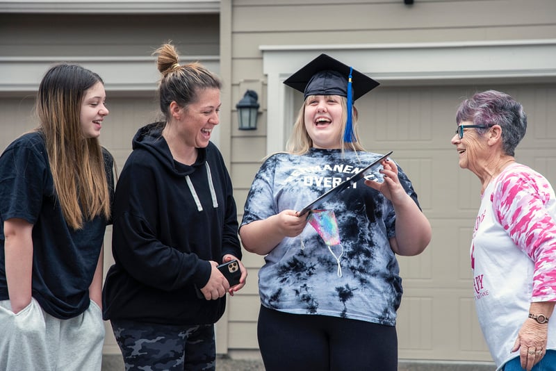 Student holds diploma and smiles in driveway surrounded by family
