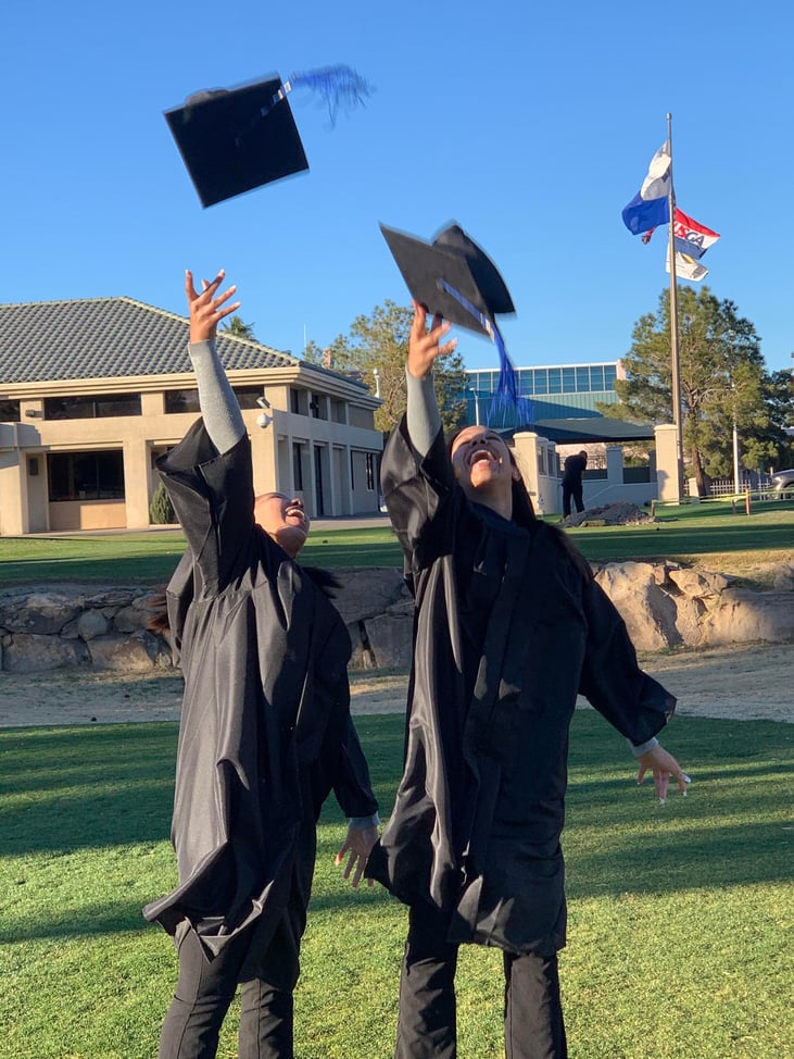 Twins stand outside and throw their graduation caps in the air