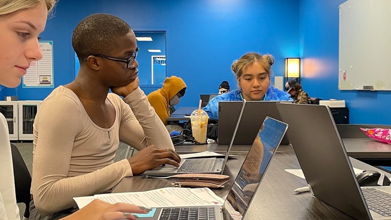 Several high school students work on laptops inside of modern work space