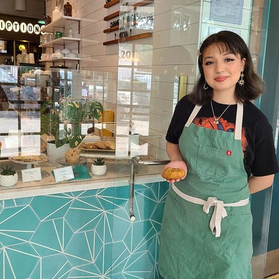 Carolina Lopez strikes a pose in her apron in front of a pastry cabinet