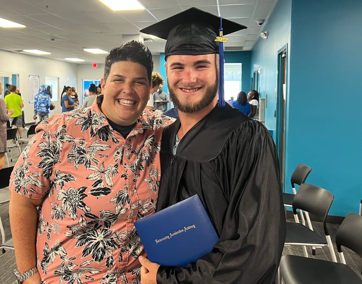 Male graduate poses inside of academy with teacher