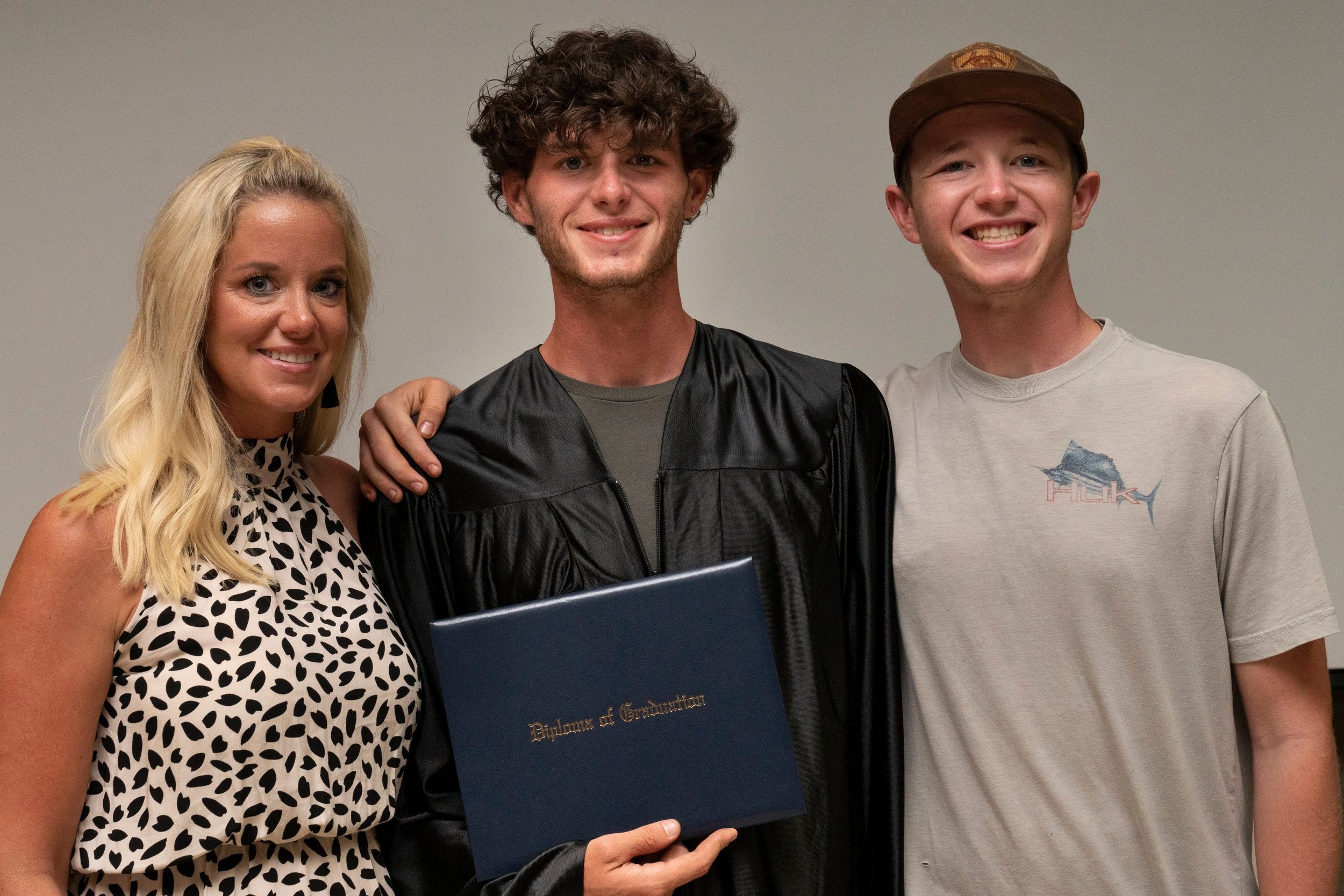 Male high school graduate poses with diploma by his family