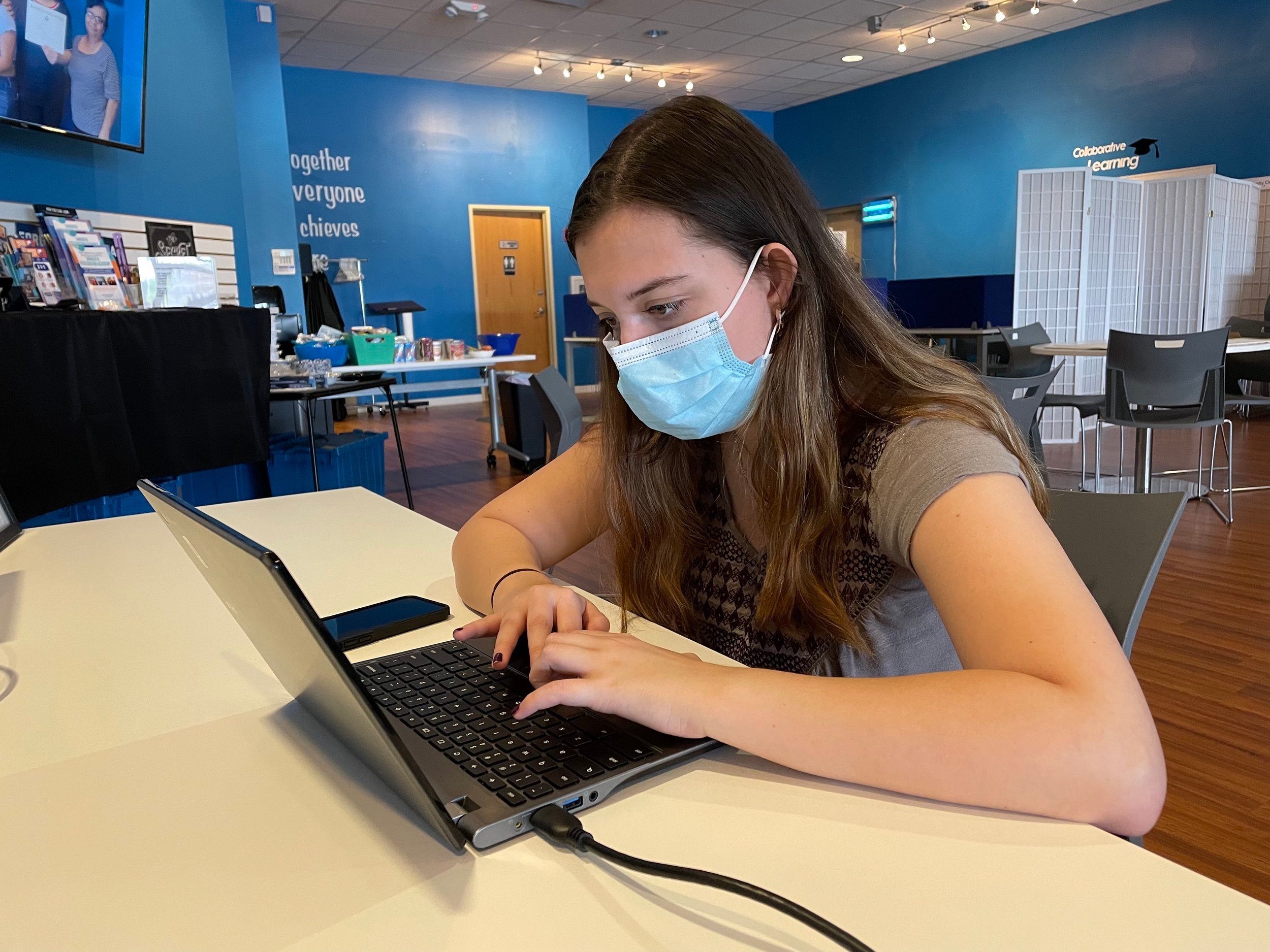 Female student in mask works on laptop