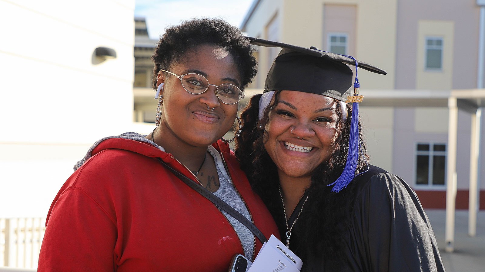 Graduate smiles alongside a family member at graduation ceremony