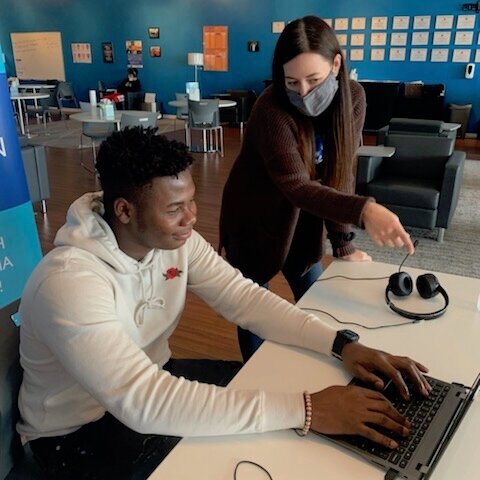 Teenager in white hoodie works on laptop with teacher helping him