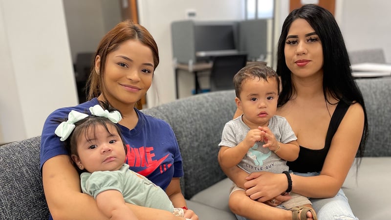Two teen moms smile with their infant children inside of an Acceleration Academies campus