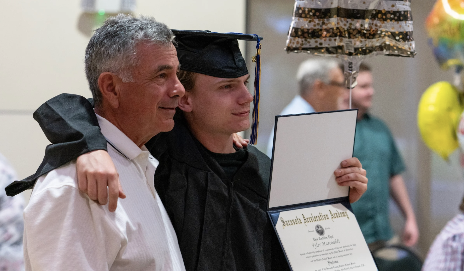 SAA grad proudly smiles at graduation with his father with diploma in hand