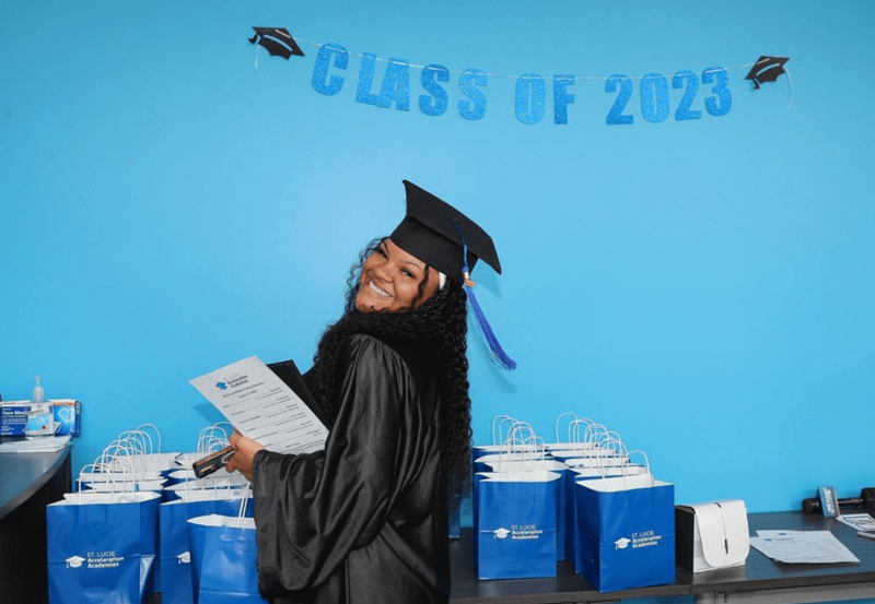 A student with a diploma smiling in front of a graduation banner